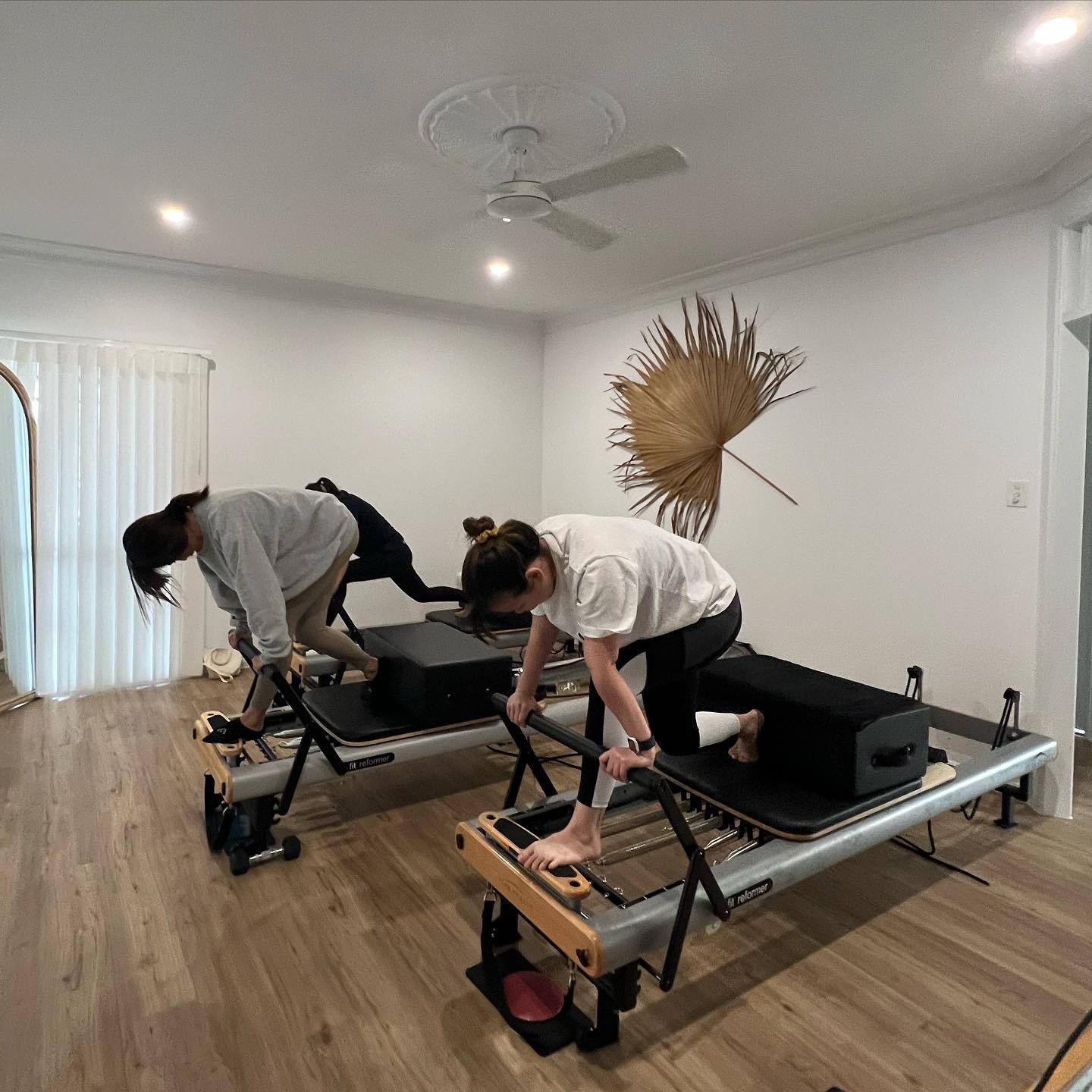 Two women mid-exercise on reformers in the Hustle studio