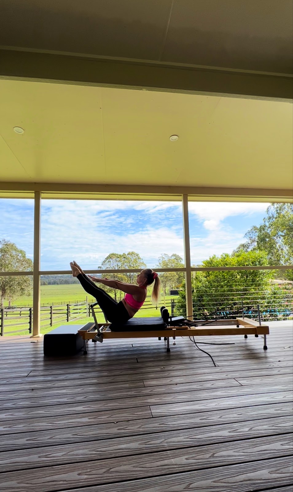 A woman holding a teaser position on a reformer on a covered deck