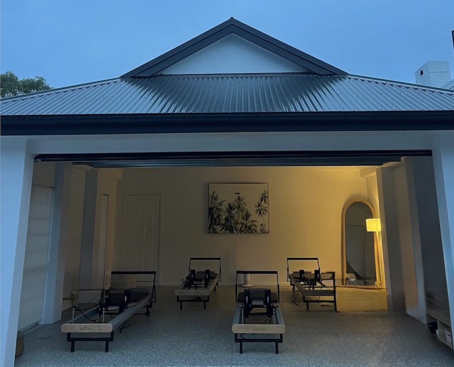The studio at dusk with its door open, four reformers inside under a warm lamp