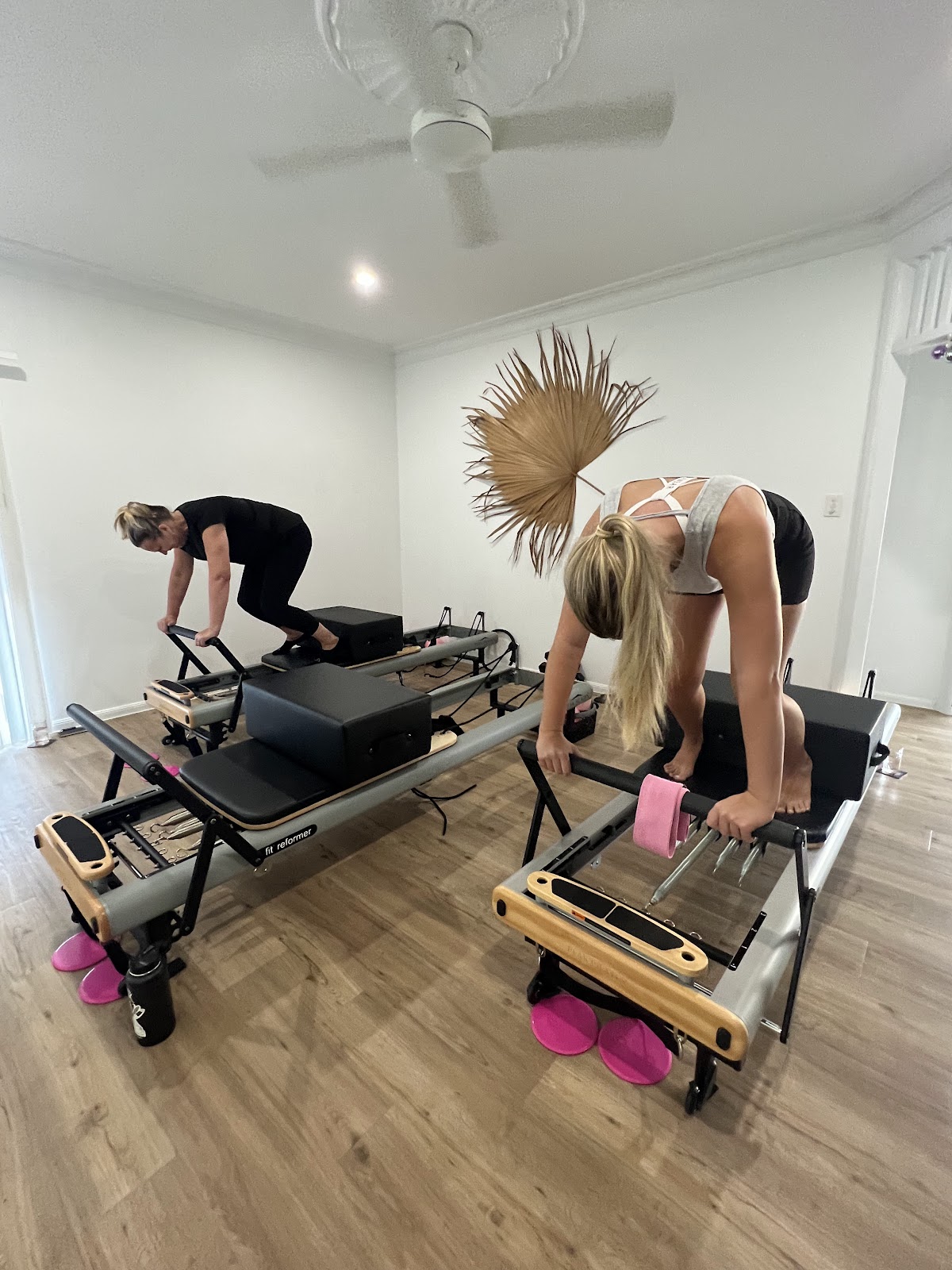A client on a reformer with pink props on the studio floor