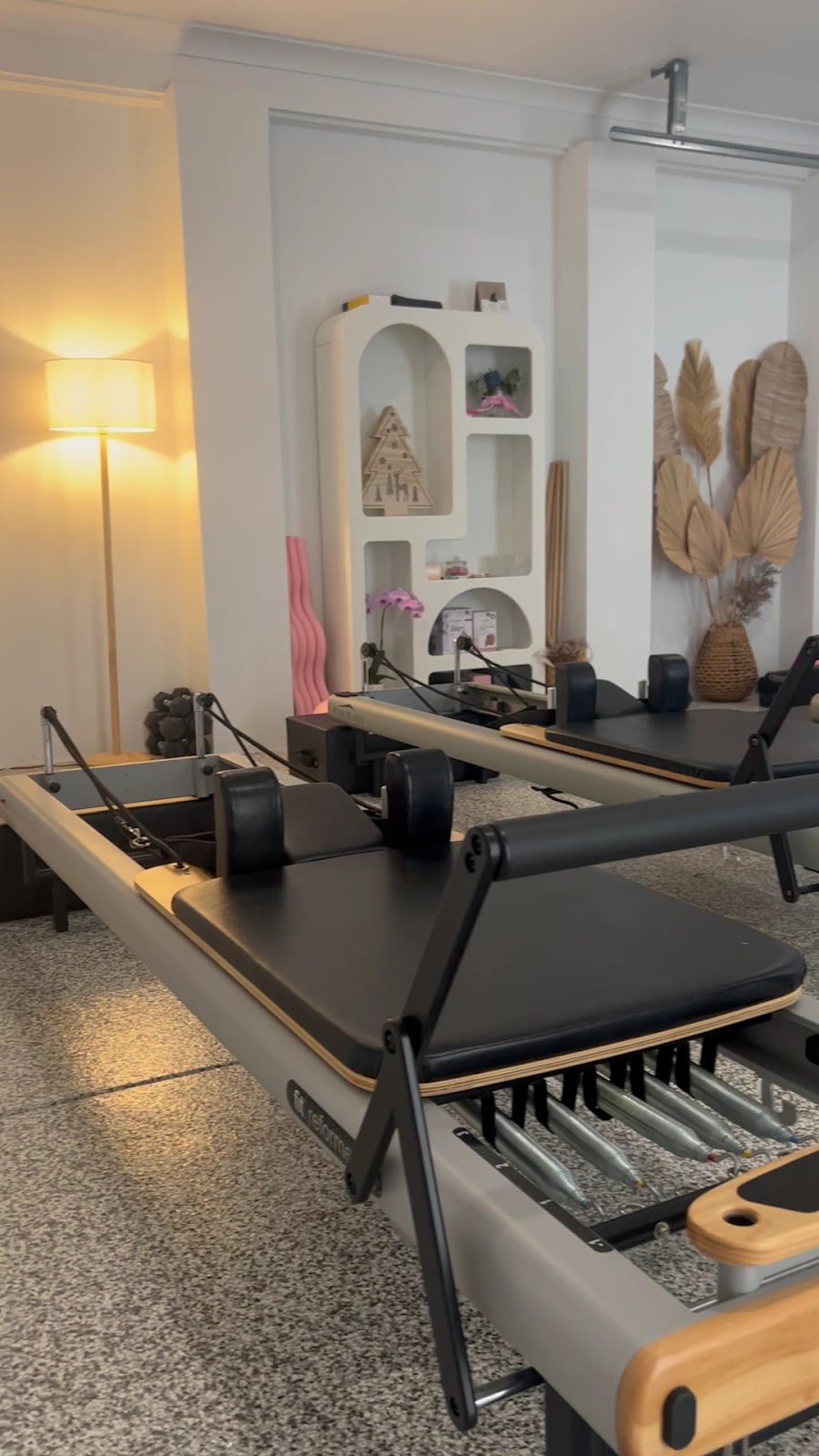 Inside the studio: a reformer, a floor lamp and shelves with dried palms